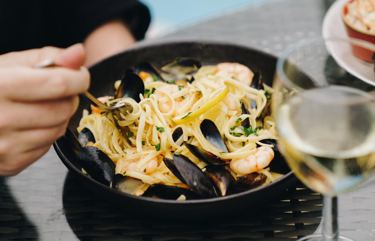 A seafood linguini dish with a glass of white wine