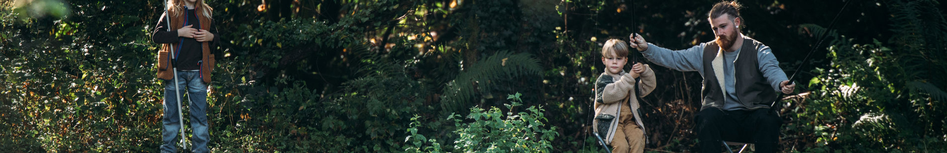 A father and two young sons fishing at a lake among woodland