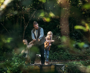A father and two young boys at a lake among woodland fishing