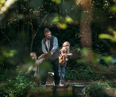 A father and two young boys at a lake among woodland fishing