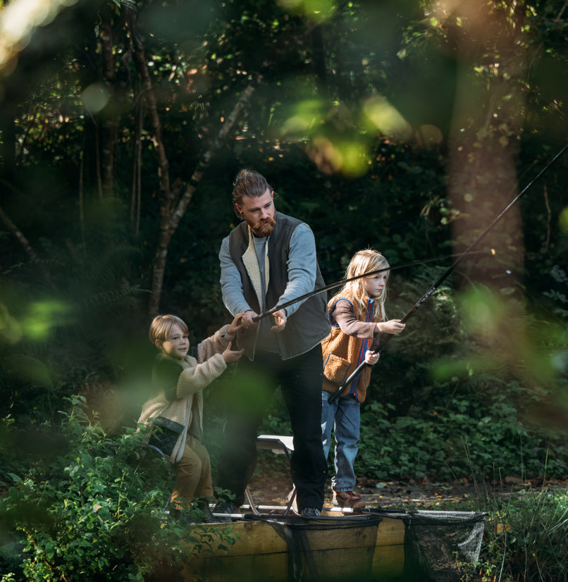 A father and two young boys at a lake among woodland fishing