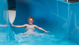 A young girl wearing goggles going down a blue indoor waterslide with a grin on her face