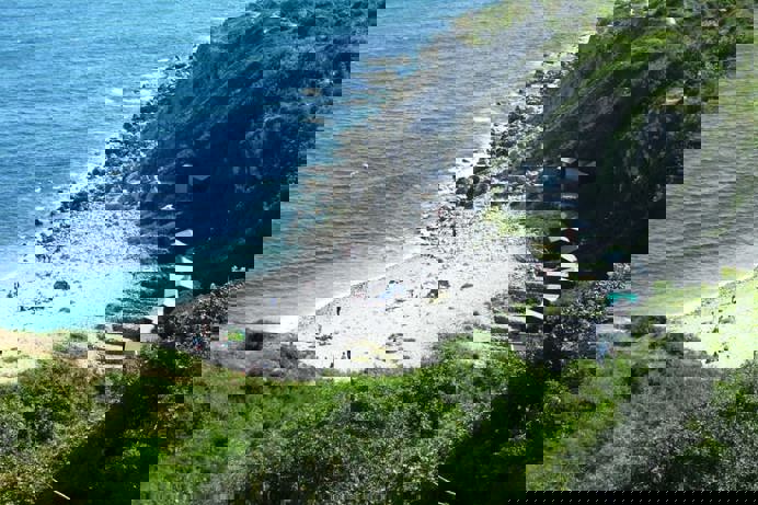 A cove with blue water down a rocky hill with various beach huts scattered