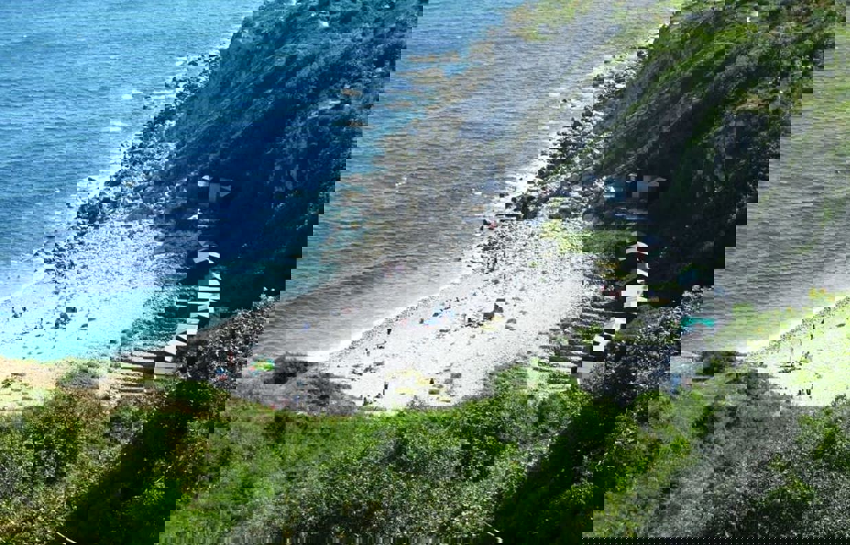 A cove with blue water down a rocky hill with various beach huts scattered