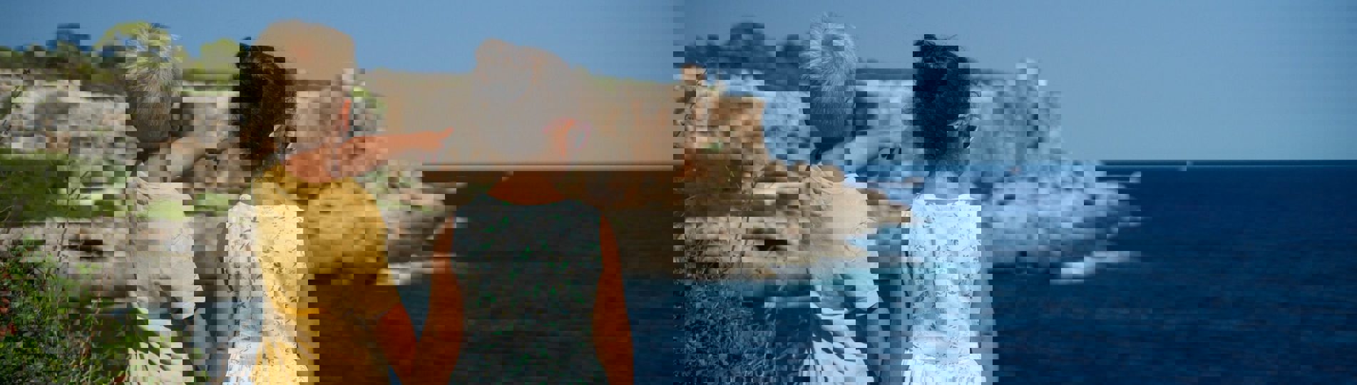 A young boy and girl standing on the edge of the coast path holding hands whilst the young boy points out to sea