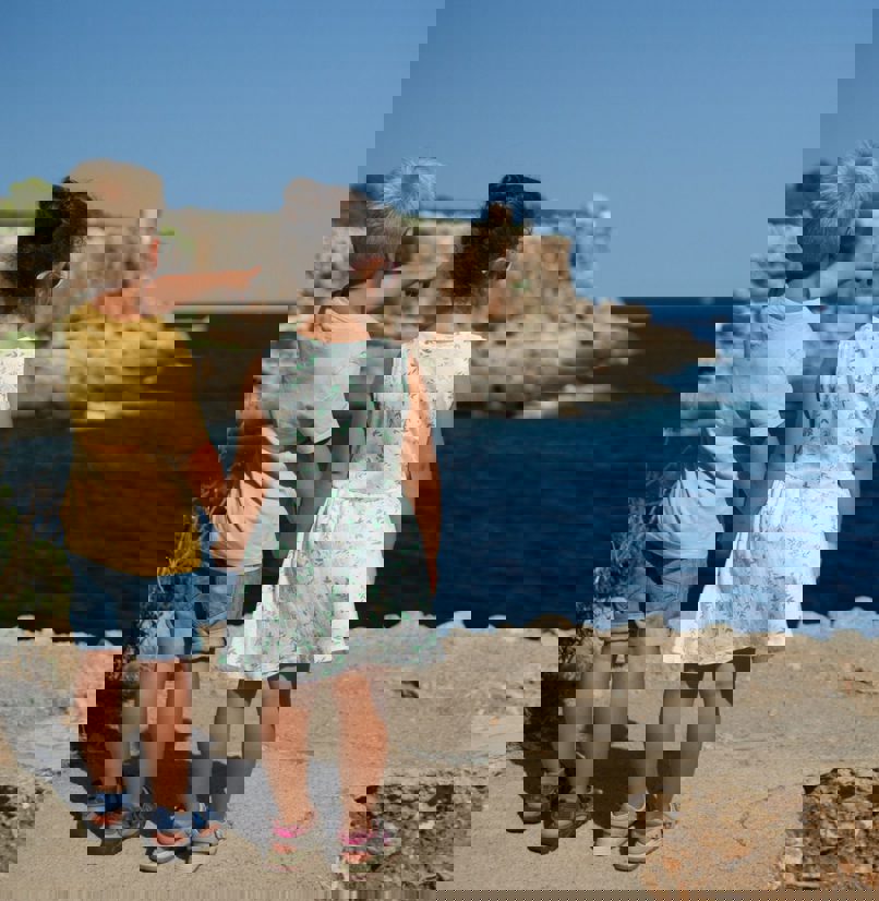 A young boy and girl standing on the edge of the coast path holding hands whilst the young boy points out to sea