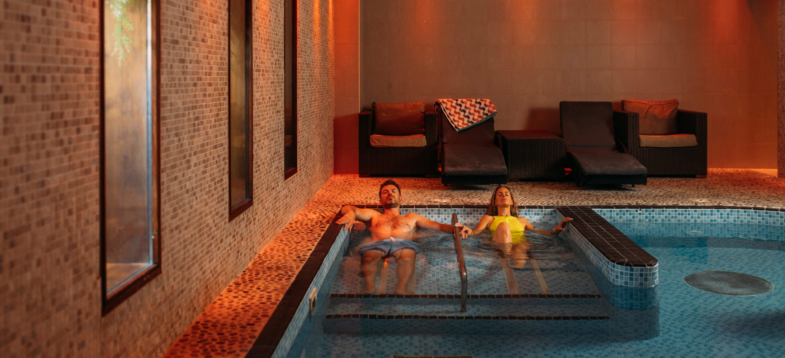 A couple laid relaxing in a hydrotherapy spa pool with loungers to sit on and calm light