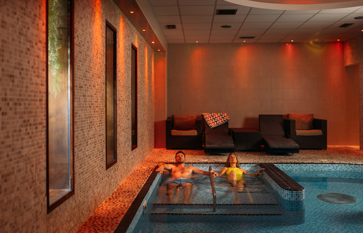 A couple laid relaxing in a hydrotherapy spa pool with loungers to sit on and calm light