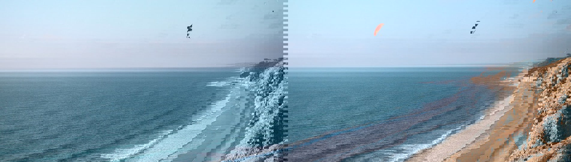 A long stretch of beach with rocky cliffs and blue waters