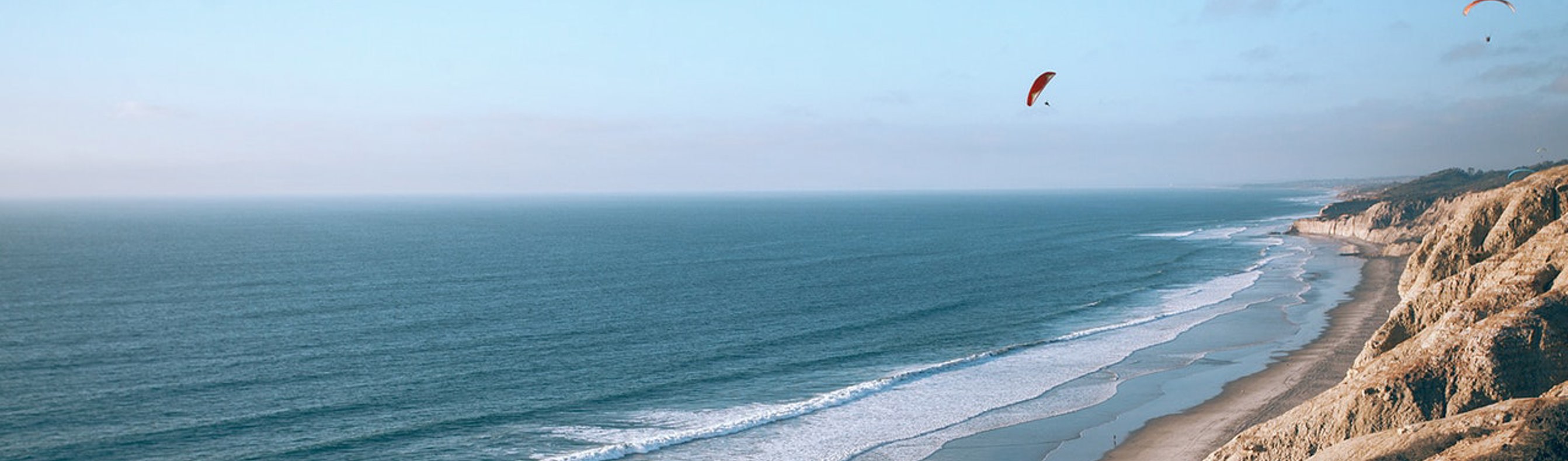 A long stretch of beach with rocky cliffs and blue waters