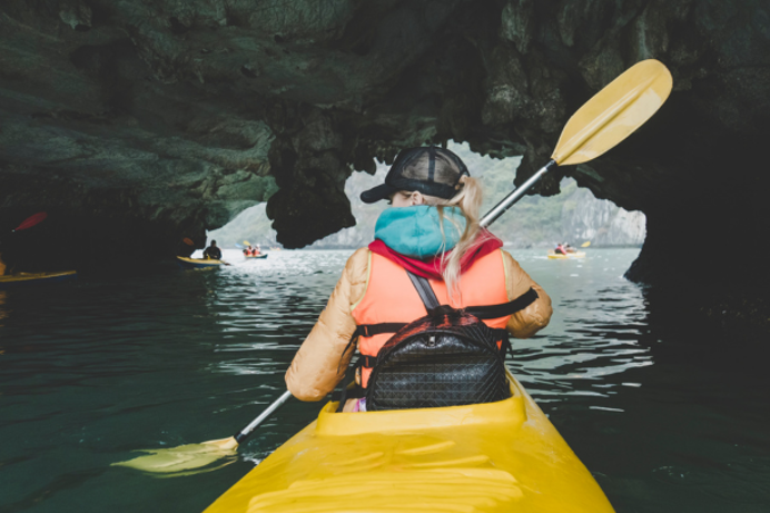 A woman paddling in a kayak under a cave