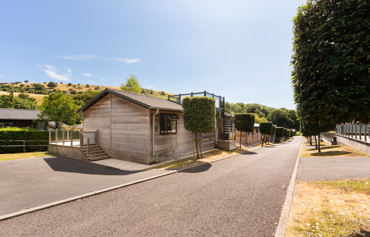 An open road on a lodge park with trees, rolling countryside hills and lodges on a sunny, blue sky day