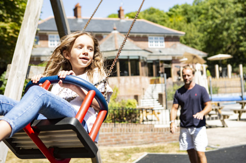 A young girl being pushed on a swing by her dad at the country club