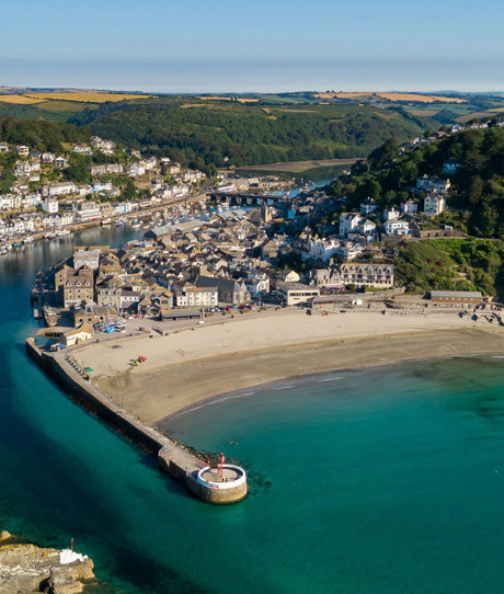 Aerial view of Looe including the beach, harbour and sea on a sunny, blue sky day