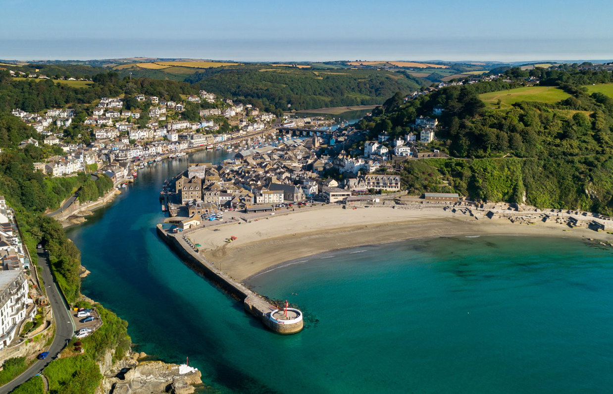 Aerial view of Looe including the beach, harbour and sea on a sunny, blue sky day