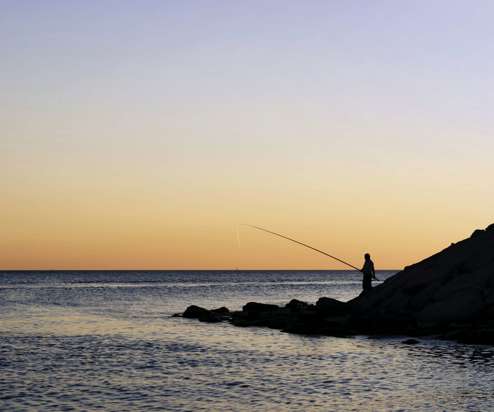 A silhouette of a person fishing in the sea with tranquil water and striking sky