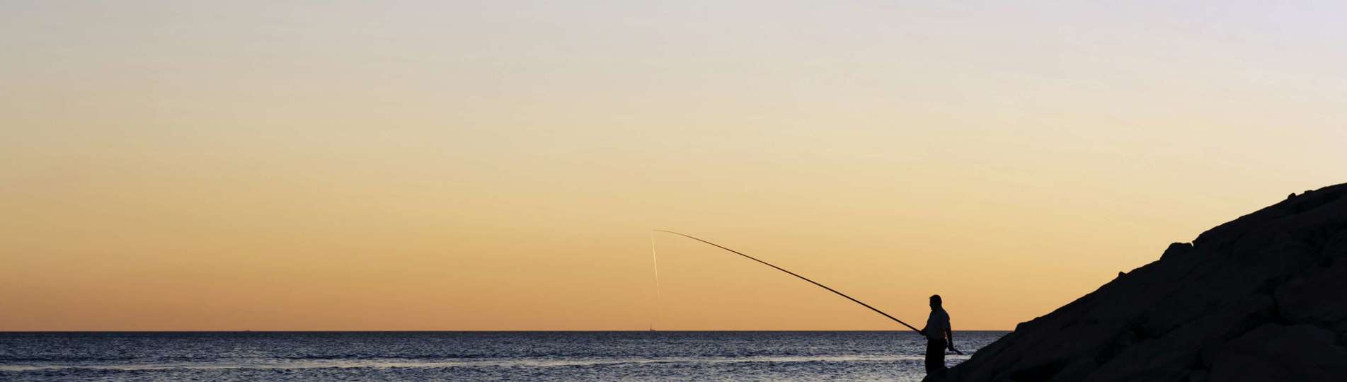 A silhouette of a person fishing in the sea with tranquil water and striking sky