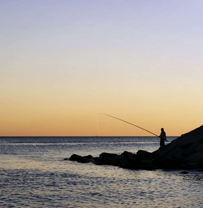 A silhouette of a person fishing in the sea with tranquil water and striking sky