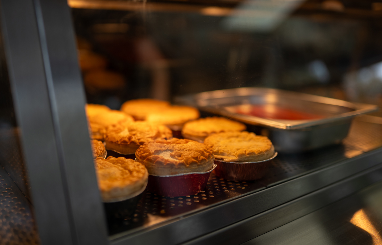 A selection of pies on a hot plate in a fish and chip shop