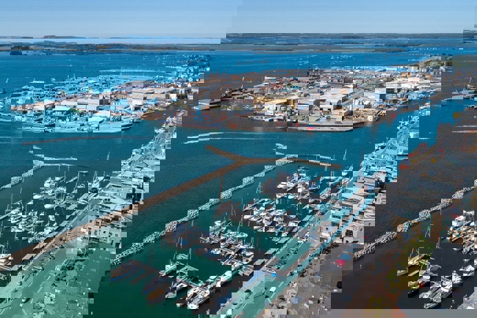 The harbour of Poole with various small boats moored on the blue waters and hills in the background