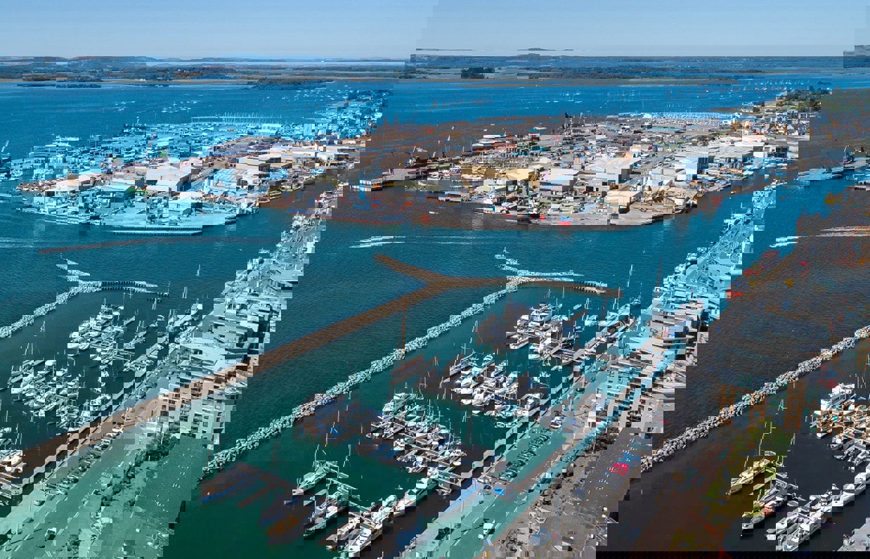 The harbour of Poole with various small boats moored on the blue waters and hills in the background