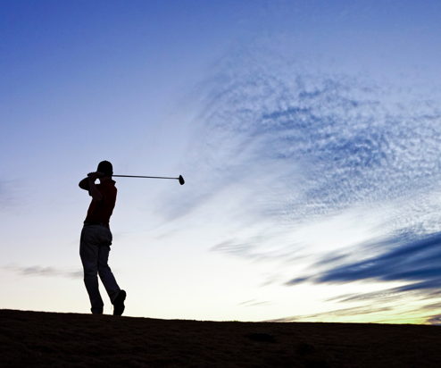 A silhouette of a man at dusk swinging a golf club