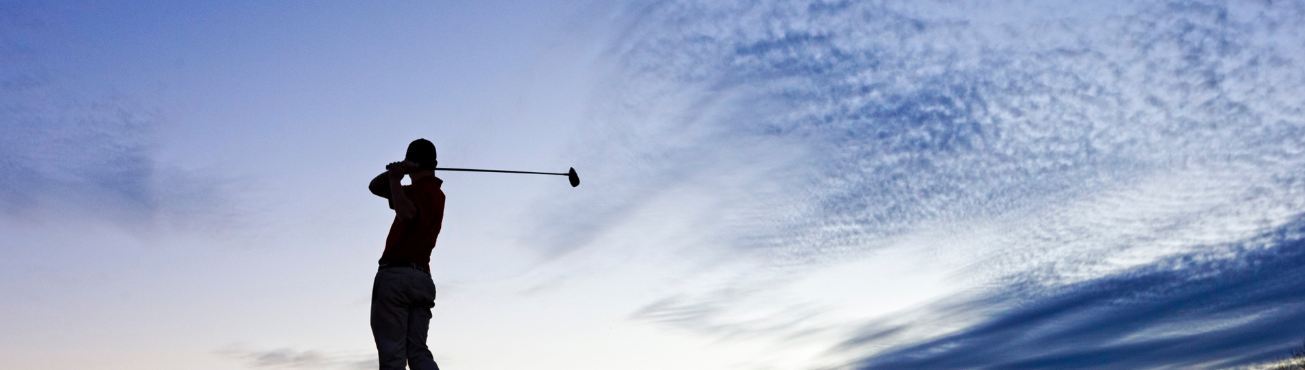 A silhouette of a man at dusk swinging a golf club