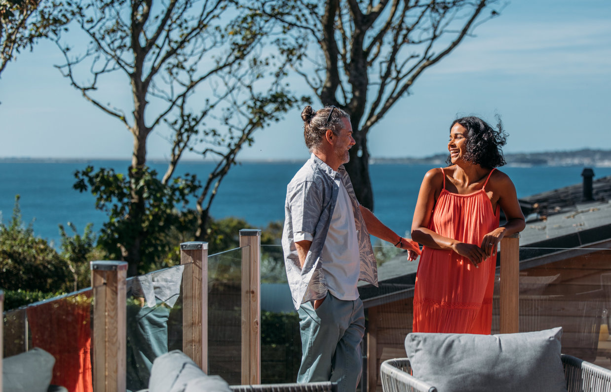 Coupe laughing together on the deck of a lodge with view of coast behind them