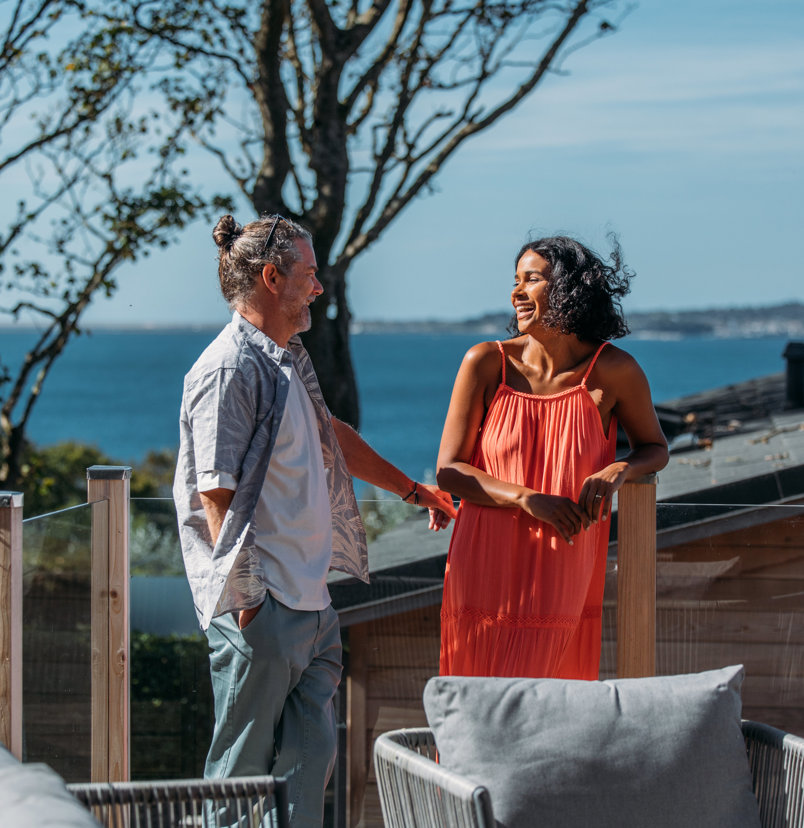 Coupe laughing together on the deck of a lodge with view of coast behind them
