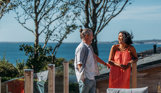 Coupe laughing together on the deck of a lodge with view of coast behind them