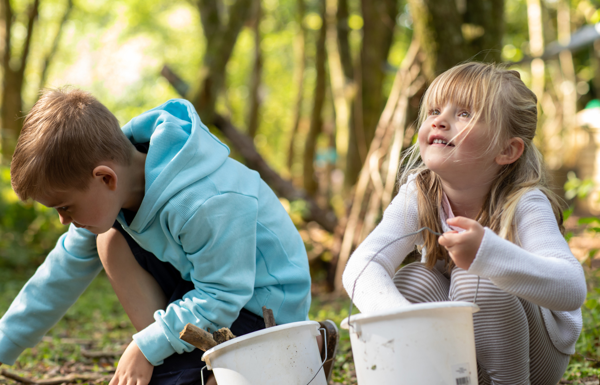 A young boy and girl collecting items in nature in buckets