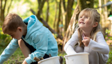 A young boy and girl collecting items in nature in buckets
