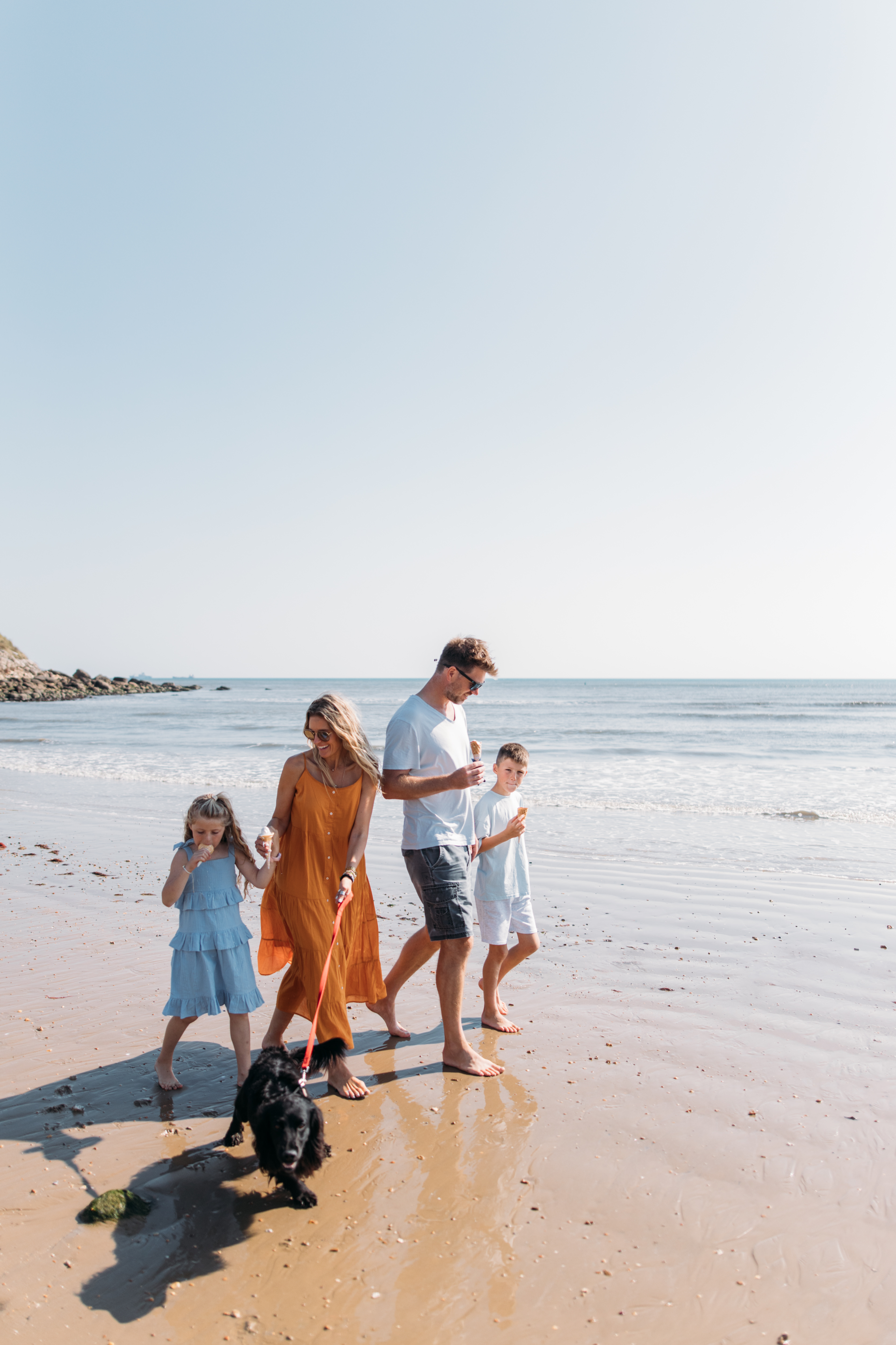 Family walking a dog on the beach eating ice creams