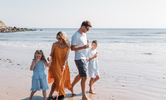 Family walking a dog on the beach eating ice creams