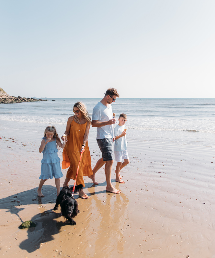 Family walking a dog on the beach eating ice creams