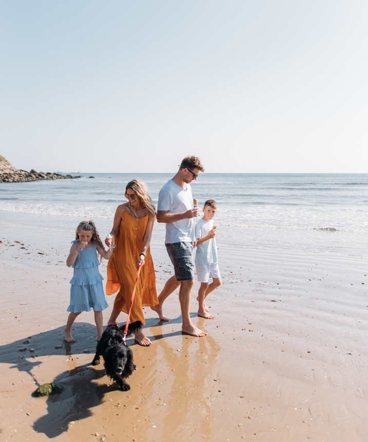 Family walking a dog on the beach eating ice creams