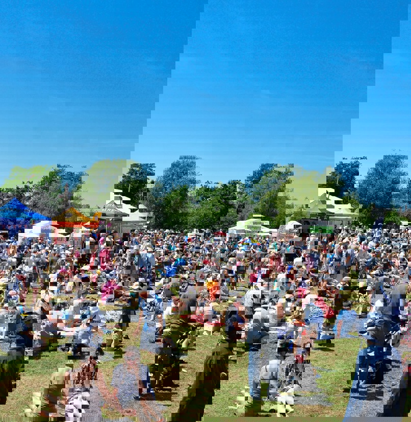 A field on a sunny day with multiple food stands and a crowd of people