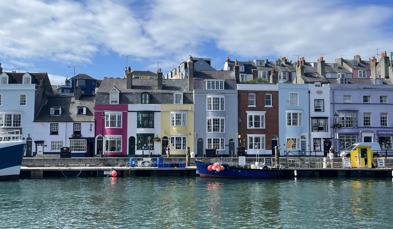 A harbour with various small boats, hills and houses on a sunny blue sky day