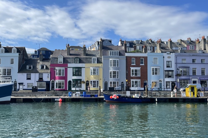 A harbour with various small boats, hills and houses on a sunny blue sky day