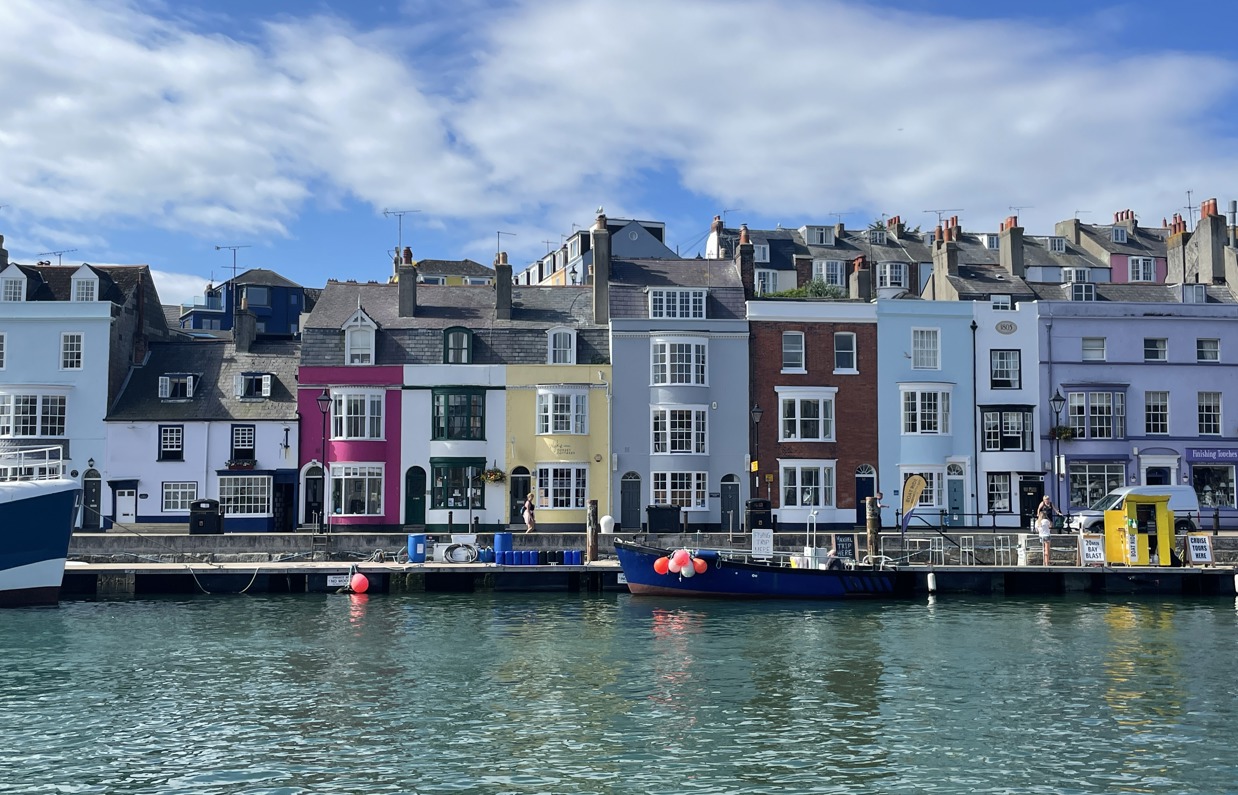 A harbour with various small boats, hills and houses on a sunny blue sky day