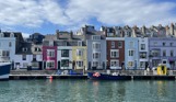 A harbour with various small boats, hills and houses on a sunny blue sky day