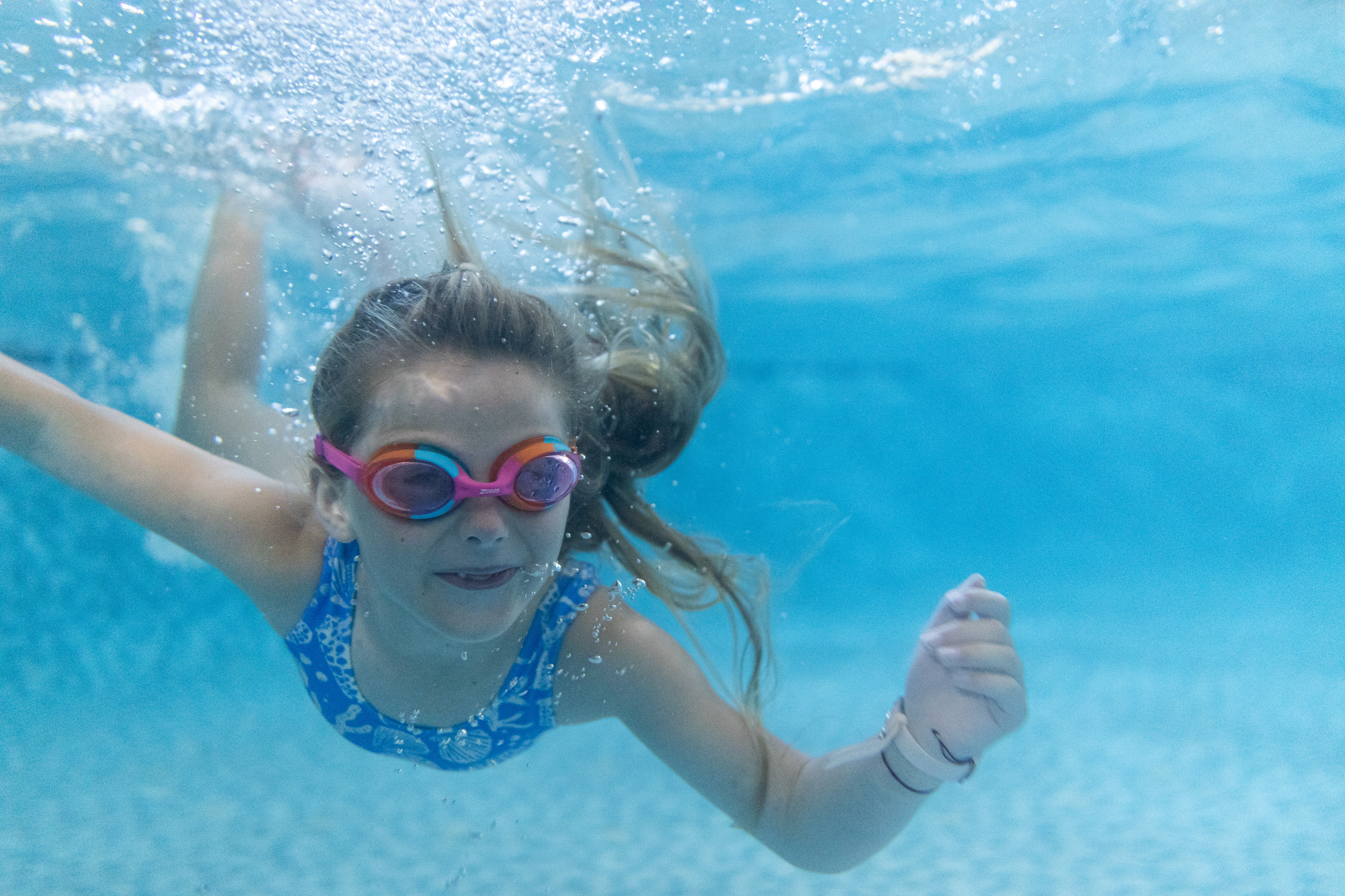 A young girl wearing goggles swimming underwater in a heated outdoor swimming pool