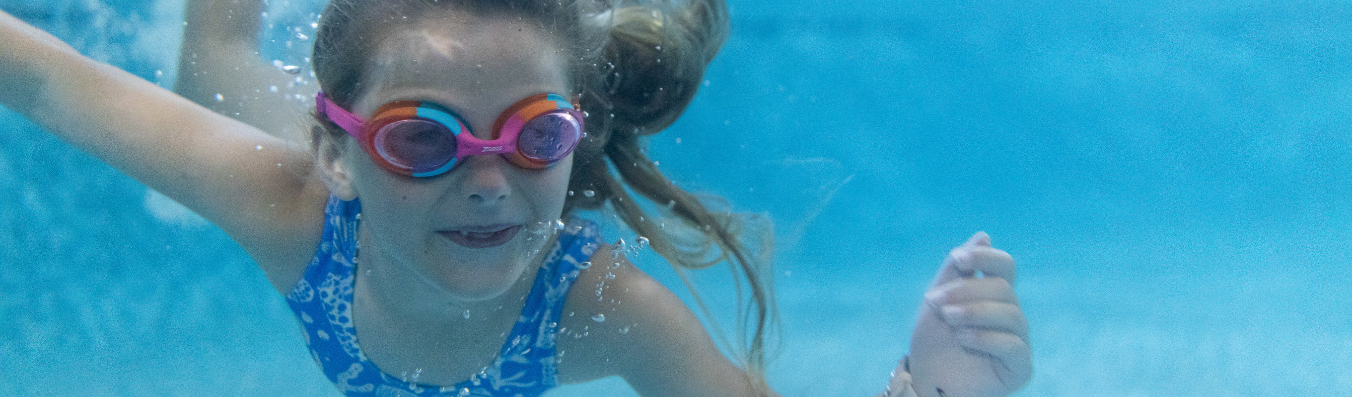A young girl wearing goggles swimming underwater in a heated outdoor swimming pool
