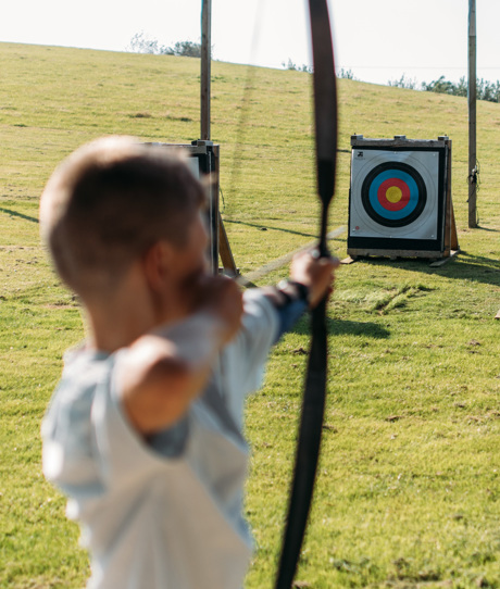 A young boy in a field aiming an archery bow at target