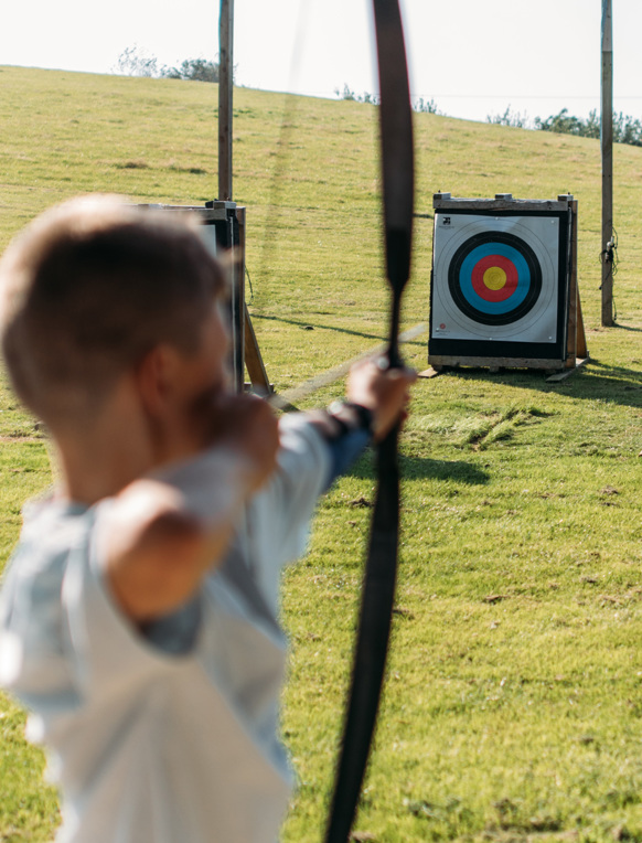 A young boy in a field aiming an archery bow at target
