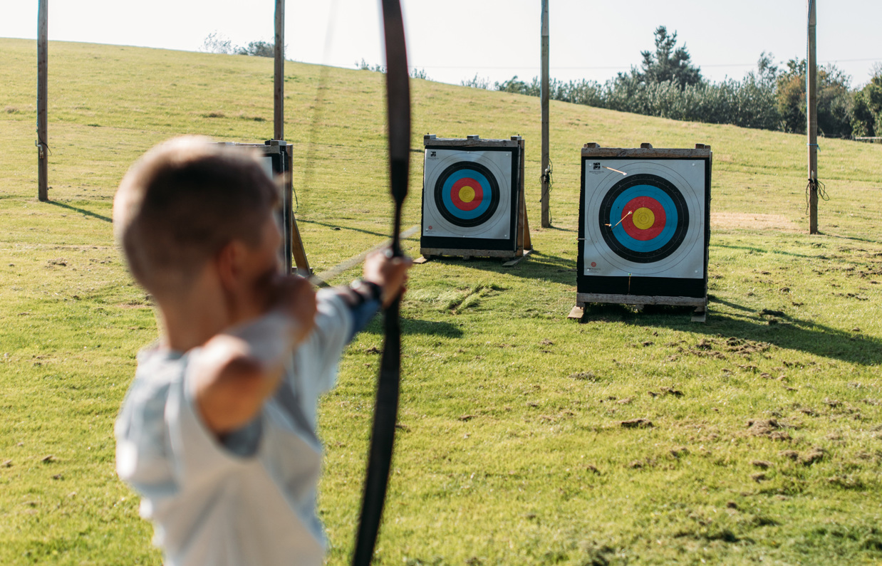 A young boy in a field aiming an archery bow at target