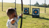 A young boy in a field aiming an archery bow at target