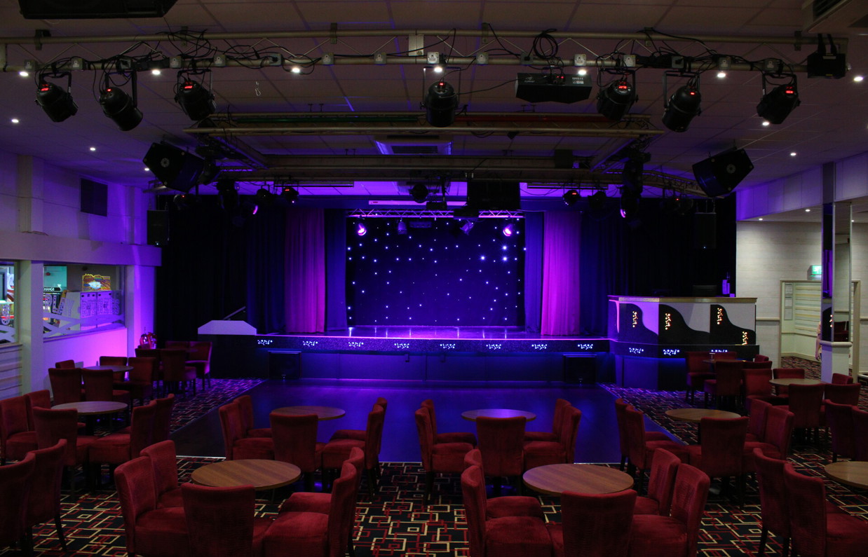 An entertainment venue with a stage and tables and chairs with lighting