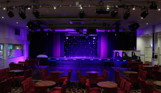 An entertainment venue with a stage and tables and chairs with lighting