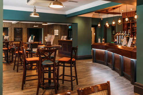 The inside of The Country Club with high tables and chairs and a bar with dramatic lighting